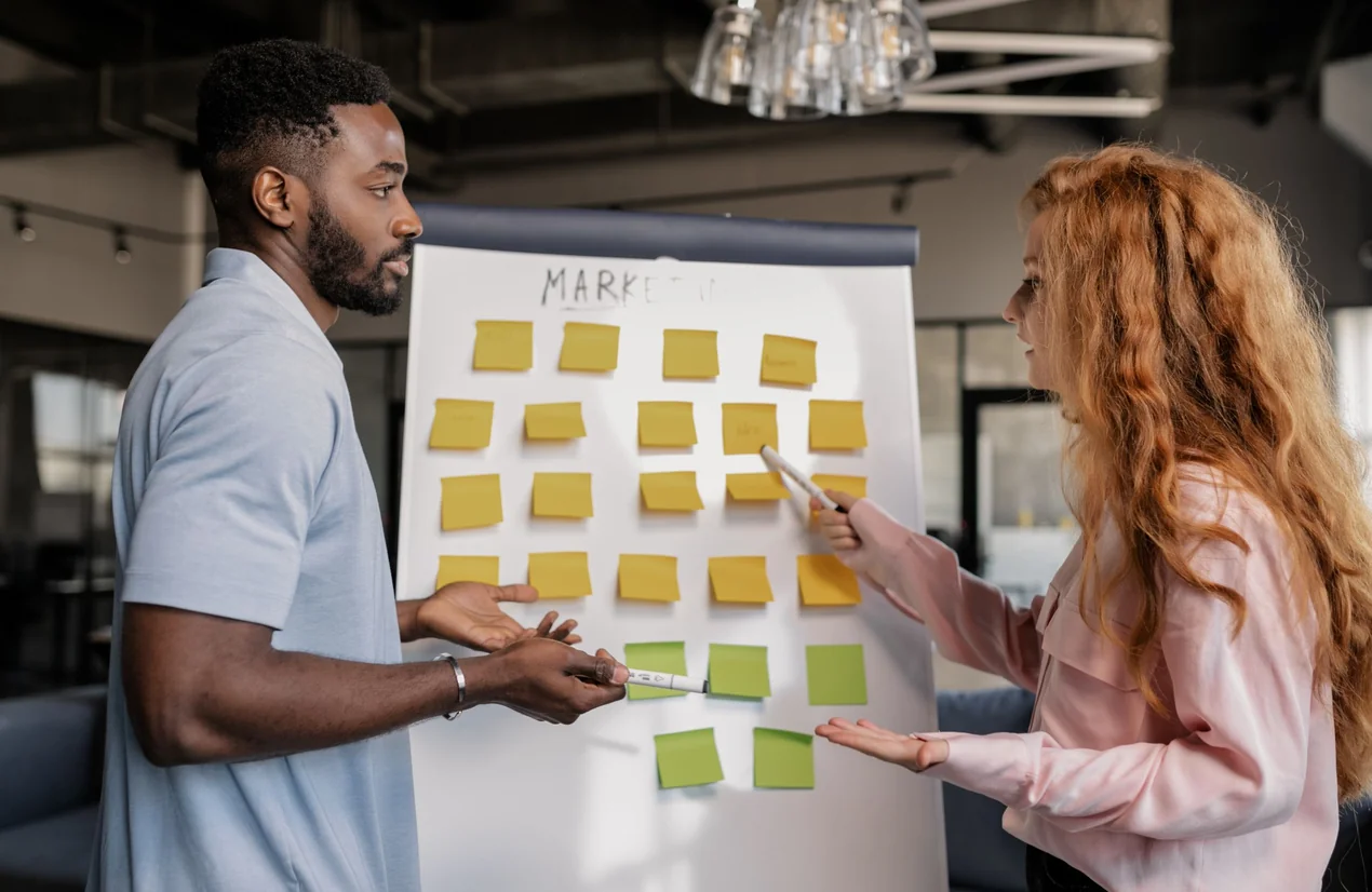 Duas pessoas a organizar ideias com post-its num painel de marketing