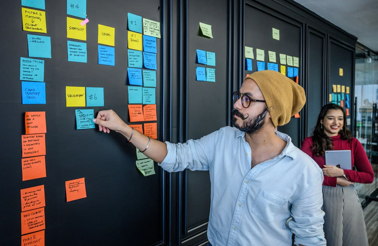 Um colega a organizar tarefas numa parede de post-its coloridos